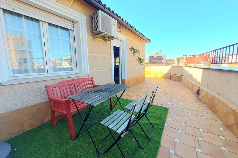 Terraza privada en la azotea con césped, banco rojo y mesa bajo el cielo azul