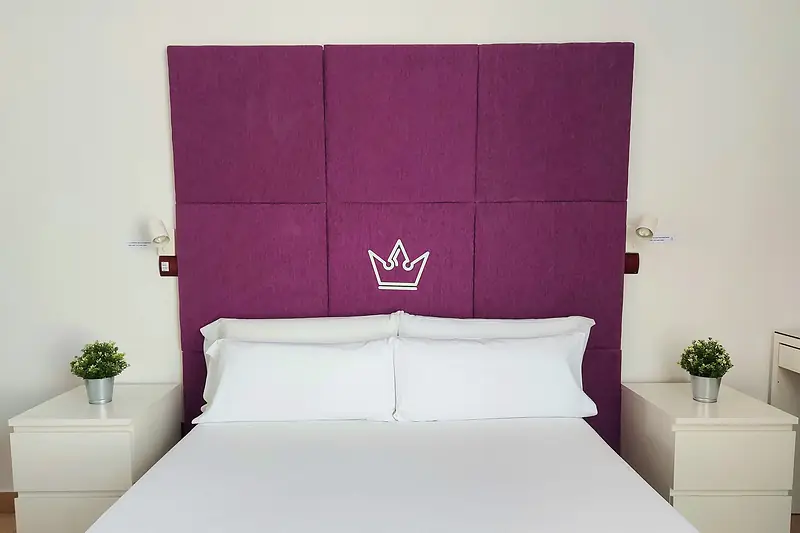 Cama de matrimonio con cabecero morado acolchado, corona y dos mesillas