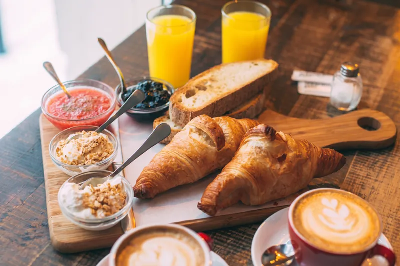 Croissants, cafés con leche y zumo de naranja en una mesa de madera