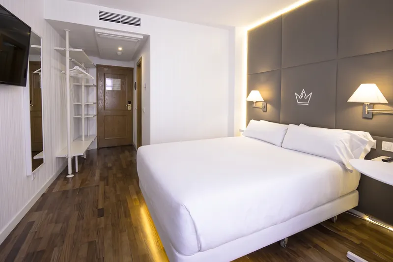 Habitación doble con cama grande, cabecero gris con corona y luz cálida bajo la cama